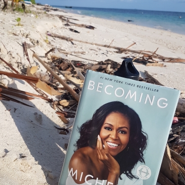 Bild zeigt einen Sandstrand mit dem Buch "Becoming" von Michelle Obama